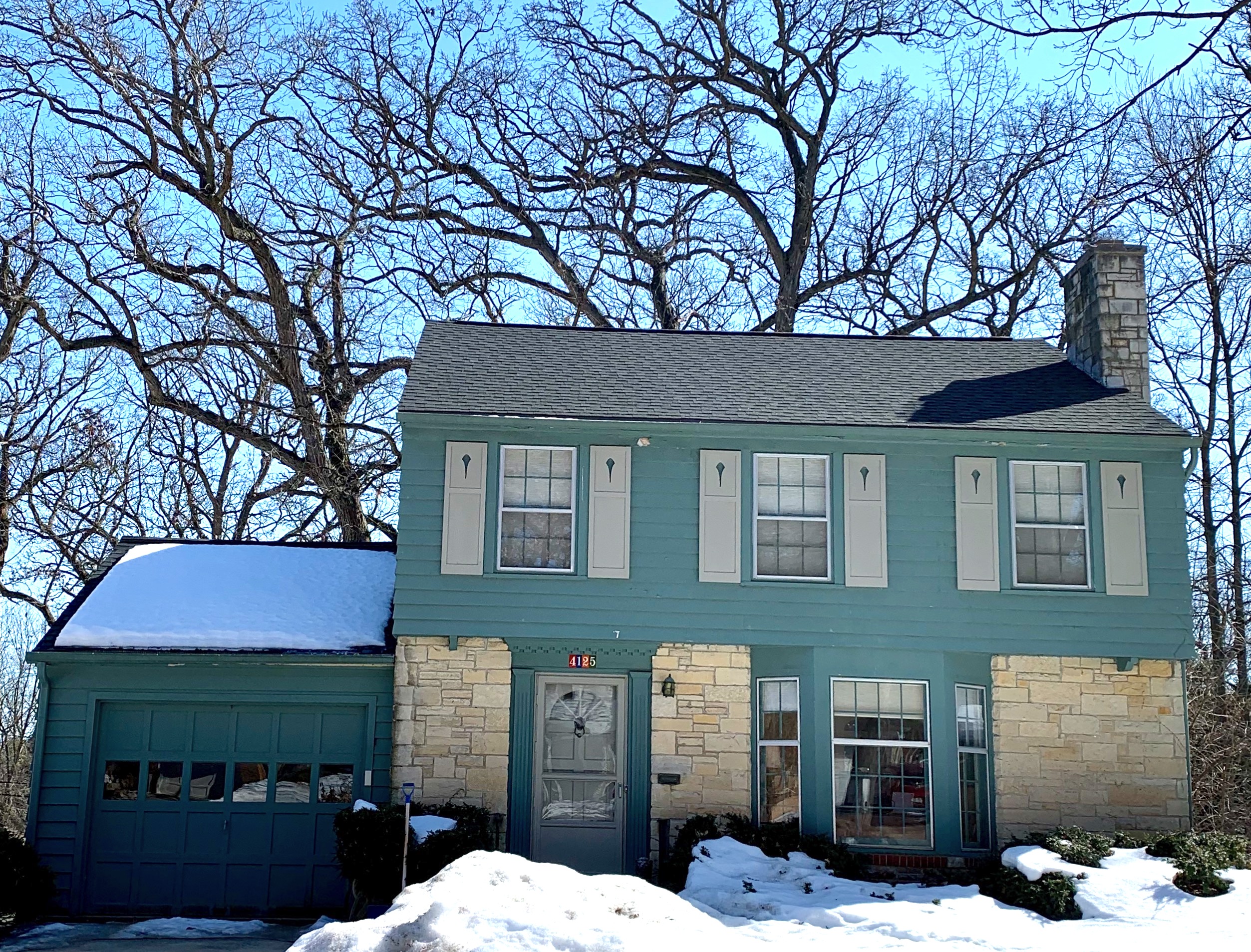 Detached two story house with flat green siding highlighted with light gray green shutters and limestone veneer
