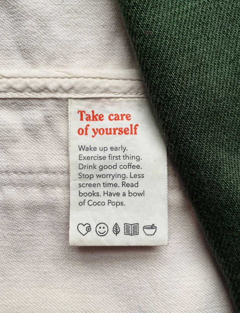 A clothing tag that says take care of yourself Wake up early. Exercise first thing. Drink good coffee. Stop worrying. Less screen time. Read books. Have a bowl of Coco Pops.